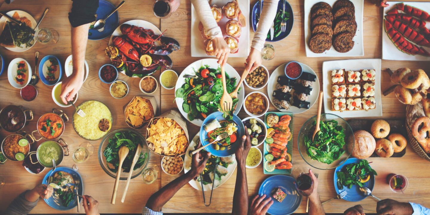 Friends sharing a meal over a table with lots of different food dishes - Food Testing Services