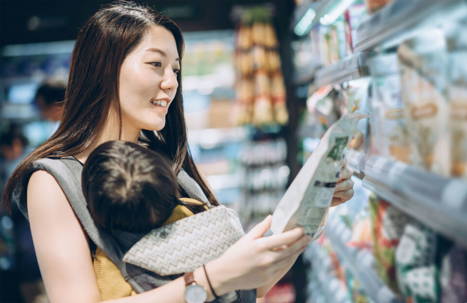 Asian mom with baby in grocery store looking at food label